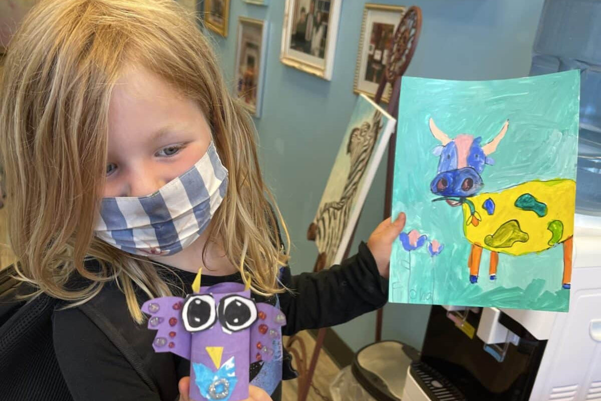 Child holding a colorful painting of a cartoon cow in an art gallery.