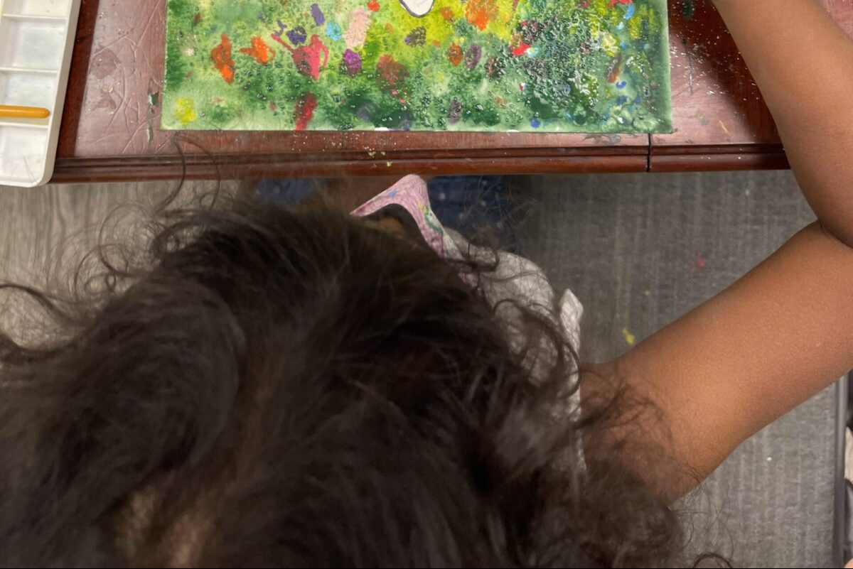 Child's colorful drawing of a house with nature elements on a wooden table.